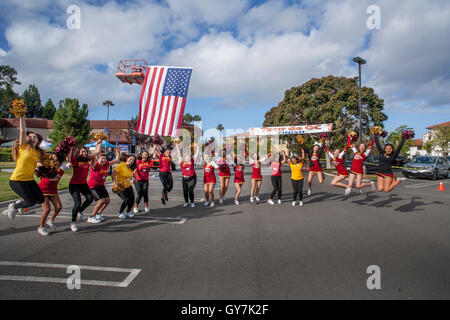 Una bandiera americana flutti nel vento come scuola locale cheerleaders salutate i ciclisti lasciando la linea di partenza di un 55-Mile fund raising carità gara in Costa Mesa, CA. Foto Stock