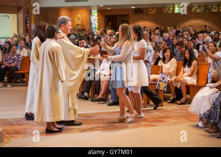 Un monsignore riceve vino sacramentale da una femmina di Prima Comunione partecipante durante una messa in una Laguna Niguel, CA, chiesa cattolica. La prima comunione è una cerimonia in alcune tradizioni cristiane durante il quale una persona riceve prima l Eucaristia. Foto Stock