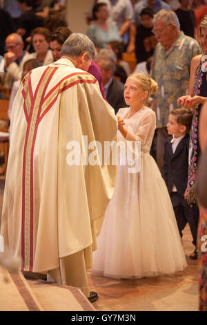 Formalmente vestiti i bambini ricevono la comunione all omelia della Santa Messa di Prima Comunione in una Laguna Niguel, CA, chiesa cattolica. La prima comunione è una cerimonia in alcune tradizioni cristiane durante il quale una persona riceve prima l Eucaristia. Nota derubato monsignor. Foto Stock