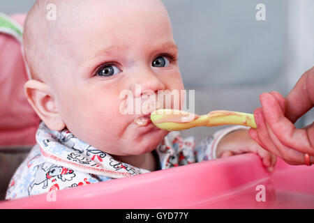 Bellissimo bambino mangia la crema di farina e di latte da mamma del canto. Egli è seduto su una rosa bambini' sedia. Foto Stock