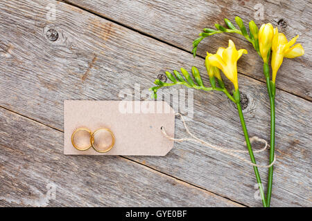 Giallo fresia fiori con tag vuoti e gli anelli di nozze sul vecchio sfondo di legno Foto Stock