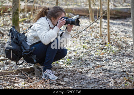 Ritratto di ben accessoriate fotografo di natura giovane donna. La ragazza takis immagini in un giorno di primavera soleggiata foresta. Foto Stock