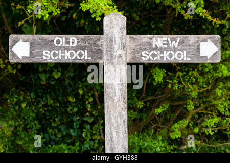 Indicazioni del cartello in legno con due frecce opposte su foglie verde dello sfondo. Vecchia scuola contro scuola nuova segnaletica direzionale Foto Stock