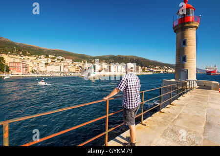 Giovane uomo attraente cercando di vecchia città di Bastia città con Joannis Babtistes cattedrale, faro e barche, Corsica Foto Stock