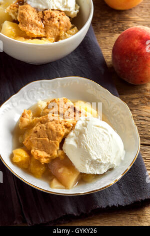 In casa peach cobbler con gelato alla vaniglia su legno rustico sfondo - sano dessert di pasticceria Foto Stock