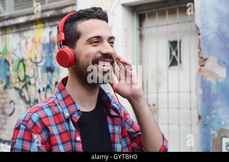 Ritratto di giovane uomo latino con red headphones. Scena urbana. Foto Stock