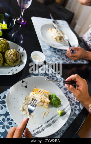 Crêpe coperti al sugo bianco giacente sulla piastra con pezzi di broccoli, uomo mangiare come visto dal di sopra, elegante Impostazione tabella Foto Stock