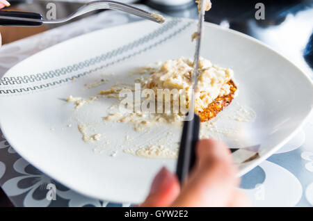 Primo piano piastra bianca con cena cremoso piatto sulla parte superiore, il coltello e la forchetta taglio in cibo Foto Stock