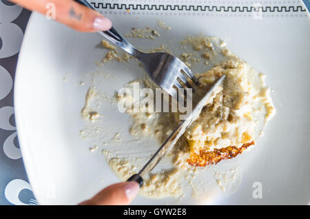 Primo piano piastra bianca con cena cremoso piatto sulla parte superiore, il coltello e la forchetta taglio in cibo Foto Stock