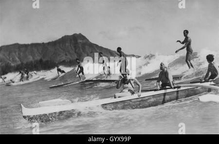 Waikiki d'epoca, vista di Honolulu sul surf, con uomini su tavole da surf in legno e donne in una barca Outrigger. Foto di Tom Blake, 1931. Foto Stock
