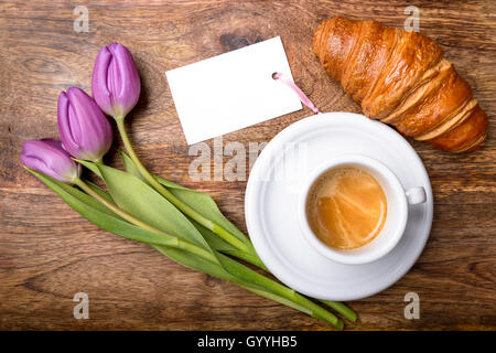 Tazza di caffè, viola i tulipani, croissant e la carta sul tavolo di legno vista superiore Foto Stock