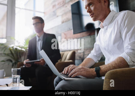 Giovane imprenditore lavorando sul portatile a riunioni aziendali. Executive maschio utilizzando laptop in riunione con colleghi aziendale di Dell Foto Stock