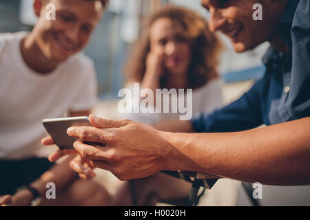 Giovani amici seduti all'aperto e guardando sullo smartphone. Gruppo di persone a guardare video sullo smartphone. Focus su mobili phon Foto Stock