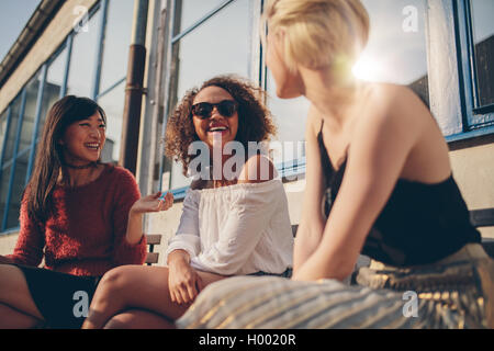 Tre giovani donne riuniti a outdoor cafe chiacchierando e gustando. Il gruppo di amici di sesso femminile avente divertimento durante la seduta in una terrazza. Foto Stock