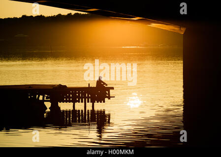 Silhouette di uomo seduto sul molo di sera la luce del sole durante la pesca. Foto Stock