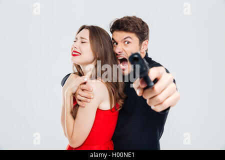 Penale furioso giovane azienda spaventata giovane donna e puntamento con la pistola su di voi Foto Stock