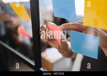 Immagine ravvicinata di mani di donna incollaggio note adesive sulla parete di vetro in office Foto Stock