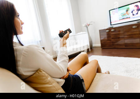 Bella giovane donna utilizzando il telecomando nella sala di pranzo e vestito elegantemente Foto Stock