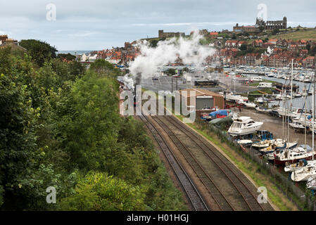 Whitby. Un North Yorkshire Moors Railway treno a vapore passa il porto, con l'abbazia e la chiesa di Santa Maria all'orizzonte. Foto Stock
