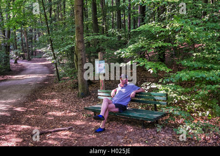 Senior uomo si siede sul banco sotto alberi ombrosi nel bosco al Lago Stechlin holiday resort, Großer Stechlinsee, Brandeburgo, Germania Foto Stock