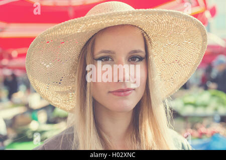 Ritratto di attraente ragazza bionda con il cappello di paglia sul Marketplace. Post elaborati con filtro vintage. Foto Stock