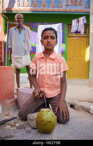 KAMALAPURAM, India - 02 febbraio 2015: ragazzo indiano aprendo una noce di cocco infront di casa in una cittadina vicino a Hampi Foto Stock