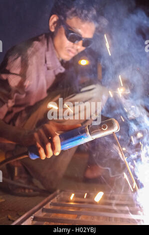 KAMALAPURAM, India - 02 febbraio 2015: lavoratore indiano la saldatura di parti metalliche pesanti su strada nel crepuscolo Foto Stock