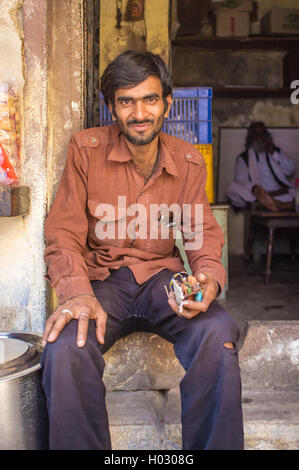 VARANASI, India - 21 febbraio 2015: Un elettricista riposa nella parte anteriore del negozio con la parte elettronica in mano. Foto Stock