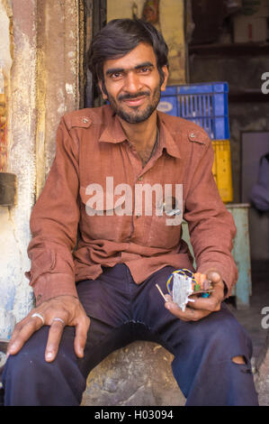 VARANASI, India - 21 febbraio 2015: Un elettricista riposa nella parte anteriore del negozio con la parte elettronica in mano. Foto Stock