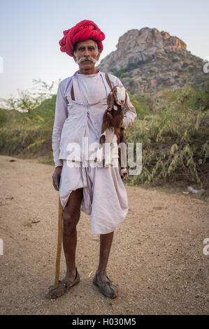 Regione GODWAR, India - 13 febbraio 2015: Anziani Rabari tribesman sorge e trattiene goatling e tradizionale ax. Rabari o Rewar Foto Stock