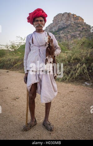 Regione GODWAR, India - 13 febbraio 2015: Anziani Rabari tribesman sorge e trattiene goatling e tradizionale ax. Rabari o Rewar Foto Stock