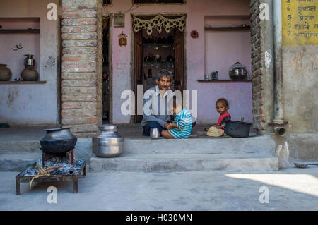 Regione GODWAR, India - 13 febbraio 2015: Padre siede dopo la prima colazione con i bambini nella porta del cortile. Foto Stock