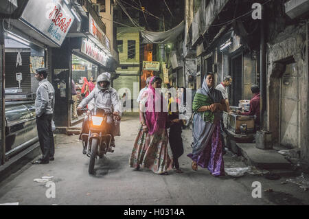 JODHPUR, India - 16 febbraio 2015: uomo sulla moto passa due donne con bambino e uomo ordinare del cibo. Post-elaborati con grano Foto Stock