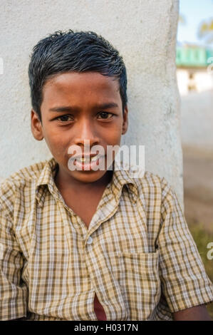 HAMPI, India - 31 gennaio 2015: Indiano ragazzo seduto in strada mentre addossato alla parete Foto Stock