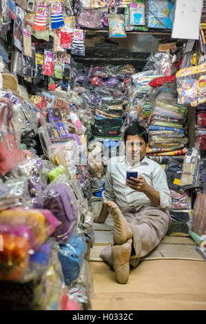 JODHPUR, India - 07 febbraio 2015: il proprietario del negozio seduto sul pavimento del negozio di abbigliamento con il telefono cellulare mentre si è in attesa per i clienti. Foto Stock