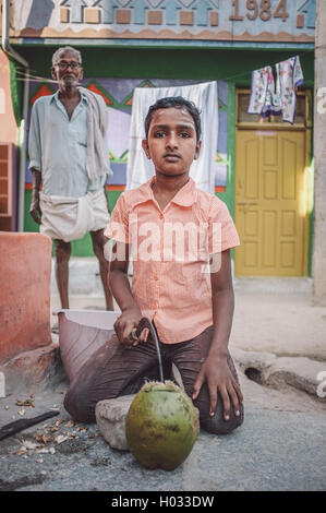 KAMALAPURAM, India - 02 FABRUARY 2015: ragazzo indiano aprendo una noce di cocco in-parte anteriore della casa in una cittadina vicino a Hampi. In Post-elaborazione w Foto Stock