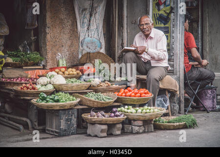 MUMBAI, India - 17 gennaio 2015: Anziani uomo indiano scrive nel libro e attende il cliente accanto al negozio di alimentari in Market street. Foto Stock