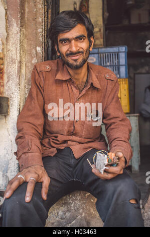 VARANASI, India - 21 febbraio 2015: Un elettricista poggia infront di shop con la parte elettronica in mano. Post-elaborati con grano Foto Stock