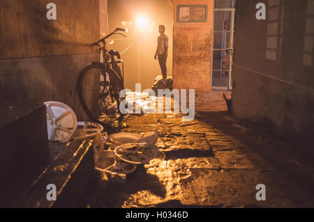 VARANASI, India - 19 febbraio 2015: uomo adulto in strada con biciclette parcheggiate e avanzi di cestino dal venditore ambulante. Post-proces Foto Stock