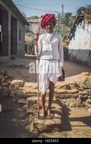 Regione GODWAR, India - 13 febbraio 2015: Rabari tribesman sorge nel cortile di casa indossando abiti tradizionali e trattiene mandria Foto Stock