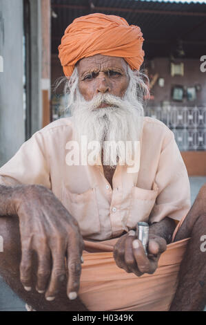 GODWAR, India - 12 febbraio 2015: Anziani tribesman indiano con turbante in lungi siede sul terreno nella parte anteriore del tempio. Post-proces Foto Stock