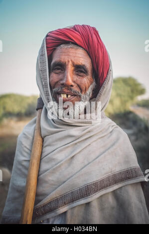 Regione GODWAR, India - 14 febbraio 2015: Anziani Rabari tribesman stand con ax su sholder. Post-elaborati con grano, tessitura Foto Stock