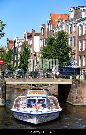 Un turista imbarcazione da diporto passando sotto uno dei molti ponti sui canali di Amsterdam Foto Stock