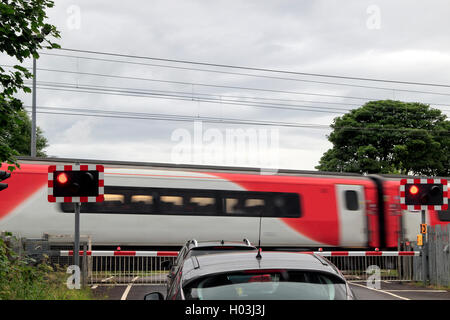 Treno che supera un passaggio a livello con il traffico in attesa presso la barriera, Northumberland, nord-est Inghilterra, Regno Unito Foto Stock