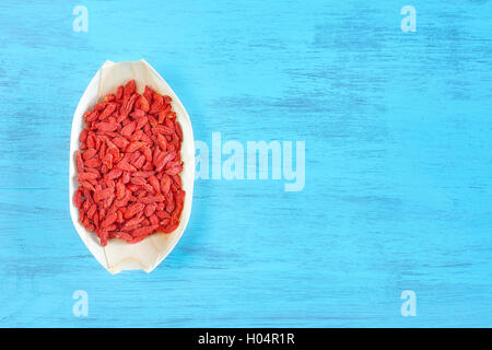 Essiccati goji bacche in una ciotola di legno su un tavolo rustico, spazio per testo, vista dall'alto. Foto Stock