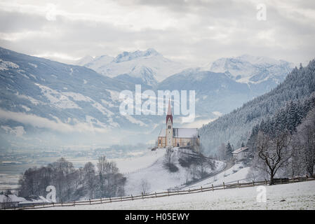 San Pancrazio chiesa in un paesaggio alpino nella neve circondato da nuvole e nebbia su una collina nella valle Zillertal, Austria. Foto Stock