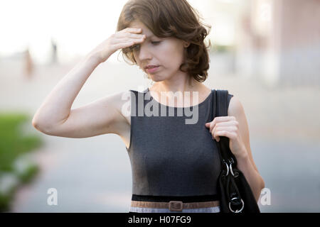 Ritratto di giovane donna ufficio camminando sulla strada in estate, accigliata, tenendo la testa con la mano, imprenditrice ha forgotte Foto Stock