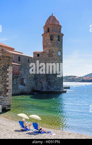 Un paio seduti su sedie a sdraio sulla spiaggia Boramar vicino alla torre di Notre Dame des Anges, Collioure, Côte Vermeille, Francia Foto Stock