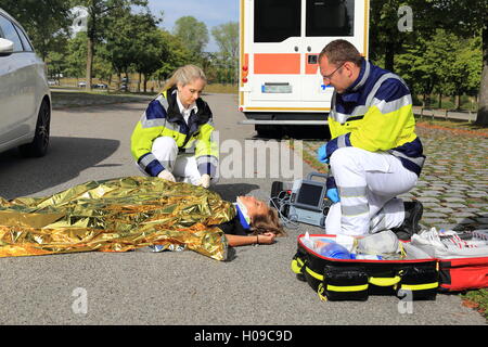 Due paramedici aiutando una donna dopo un incidente di traffico Foto Stock