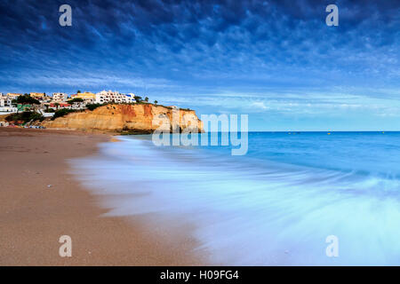 Oceano onde che si infrangono sulle rocce e spiaggia che circonda il villaggio di Carvoeiro al tramonto, Lagoa comune, Algarve, Portogallo, Europa Foto Stock